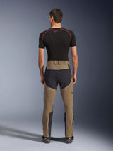 Alpinestars Flex-AST Explorer broek, Walnut Black, achteraanzicht op model, met versterkt zwart zitvlak en bruin stretchtextiel, gecombineerd met een zwarte base layer en technische motorlaarzen, duurzame adventure motorkleding