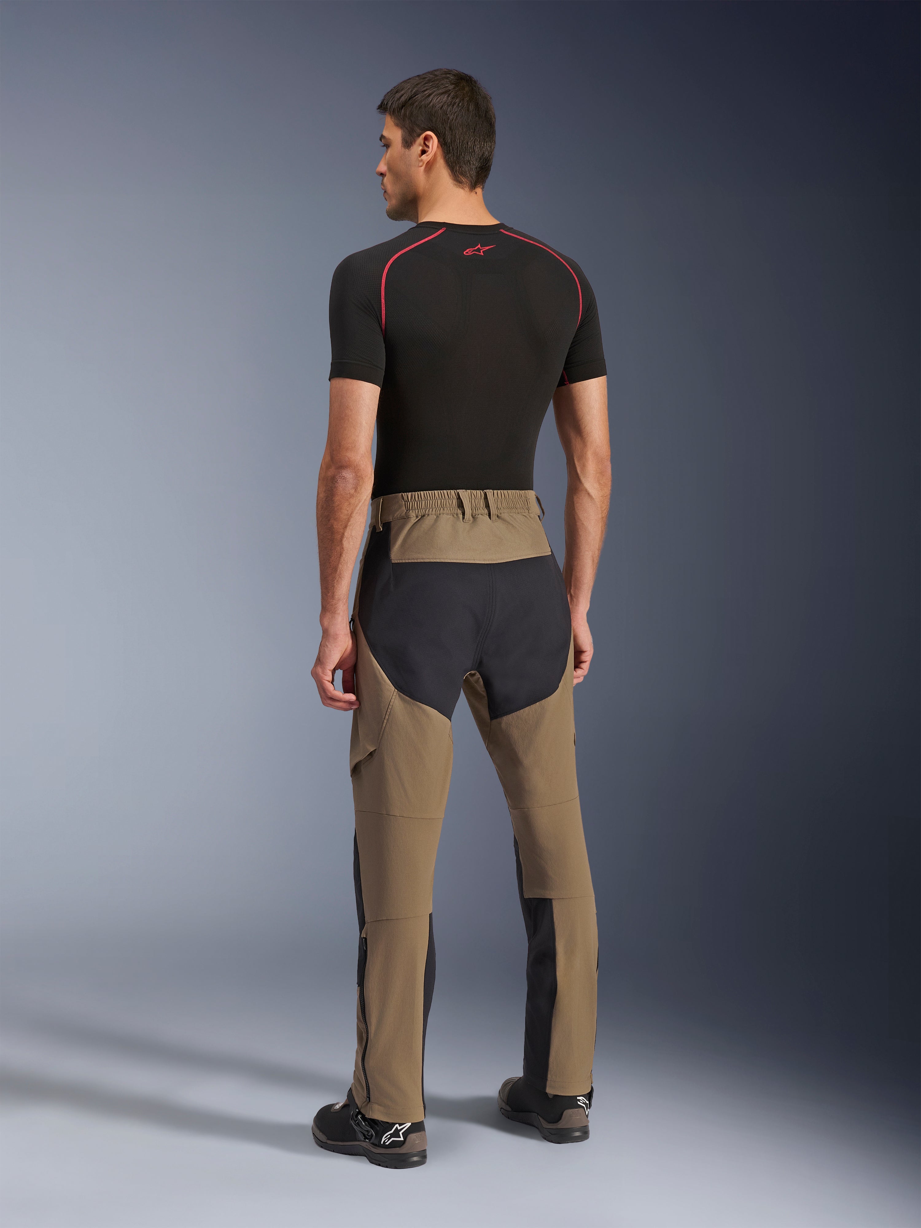 Alpinestars Flex-AST Explorer Broek, adventure motorbroek, Walnut Black, achteraanzicht op model met zwarte ripstop-panelen op het zitvlak en de benen, stretch textielconstructie en lange ritsen aan de onderbenen voor adventure touring