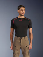 Alpinestars Flex-AST Explorer broek, adventure motorbroek, Walnut Black, gedragen door een model met een zwart base layer shirt, voorzien van diagonale cargozakken met ritssluiting en een duurzame stretch textielconstructie.