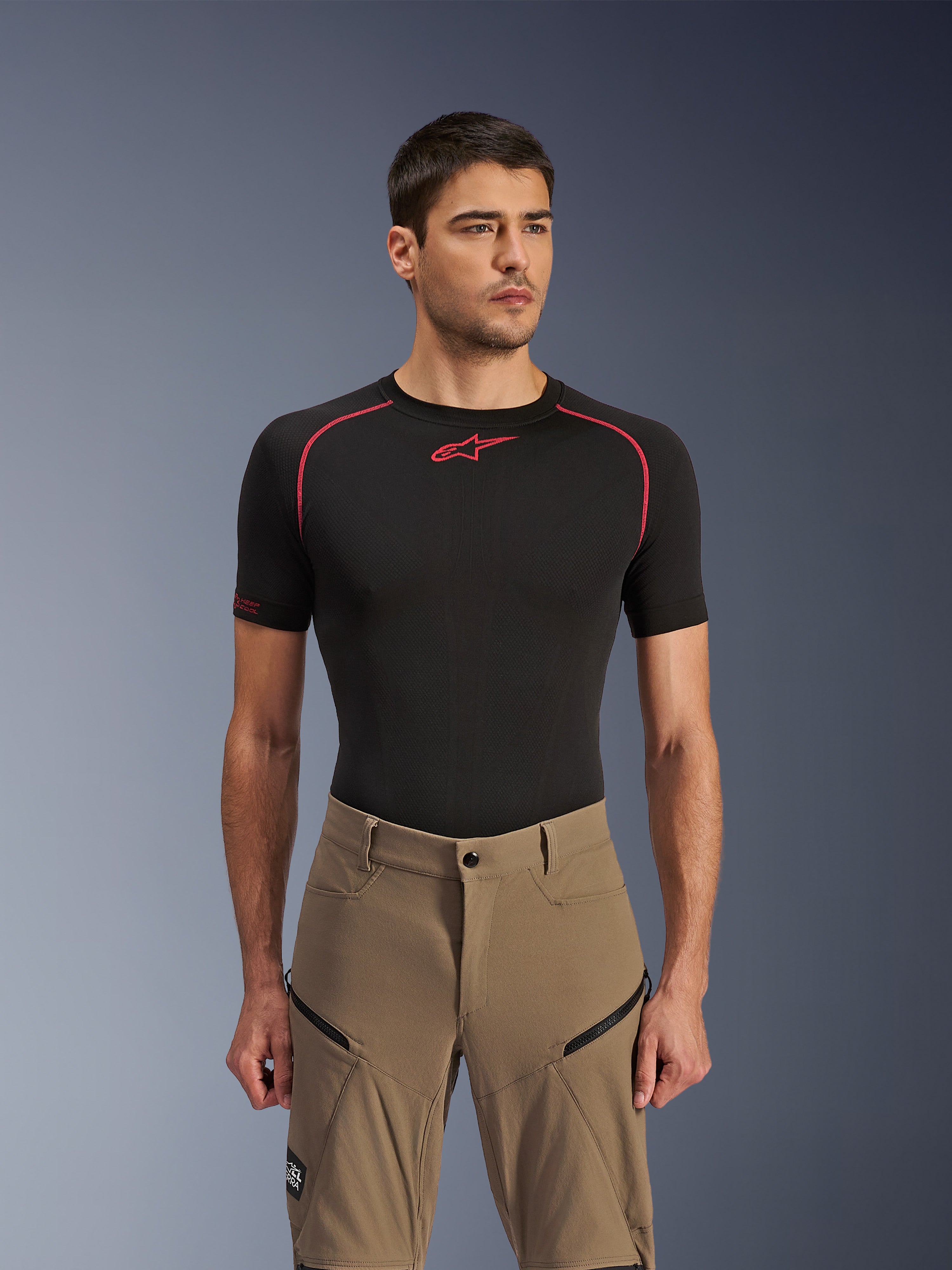 Alpinestars Flex-AST Explorer broek, adventure motorbroek, Walnut Black, gedragen door een model met een zwart base layer shirt, voorzien van diagonale cargozakken met ritssluiting en een duurzame stretch textielconstructie.