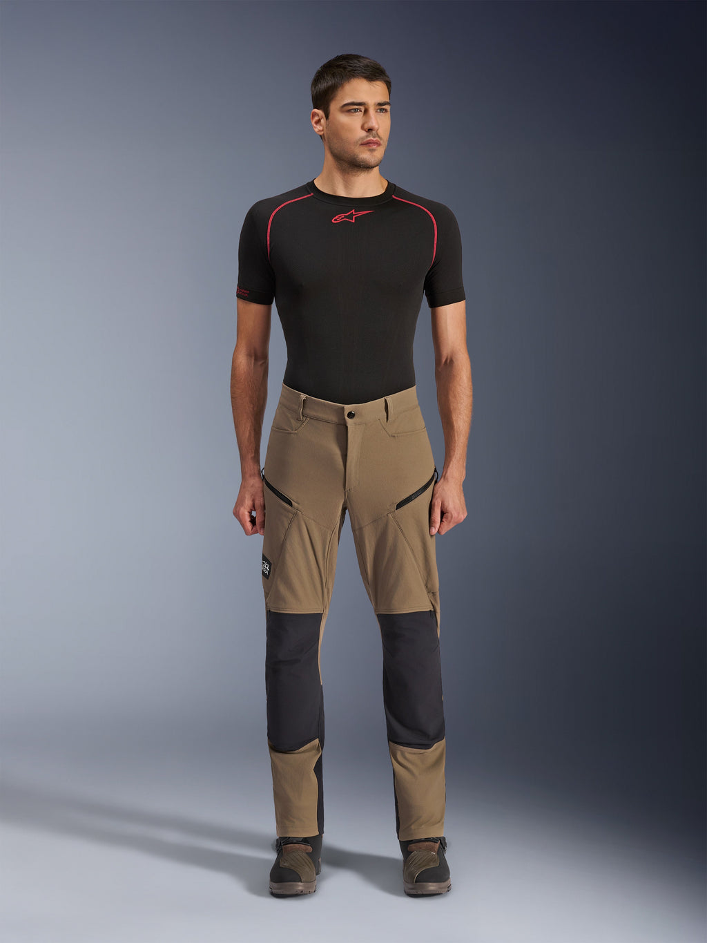 Alpinestars Flex-AST Explorer broek, motor touringbroek, walnootbruin en zwart, voorzien van verstevigde kniepanelen en dijbeenzakken met rits, gedragen met een zwarte basislaag met korte mouwen, volledig lichaamsaanzicht
