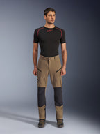 Alpinestars Flex-AST Explorer broek, motor touringbroek, walnootbruin en zwart, voorzien van verstevigde kniepanelen en dijbeenzakken met rits, gedragen met een zwarte basislaag met korte mouwen, volledig lichaamsaanzicht