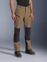 Alpinestars Flex-AST Explorer broek, adventure motorbroek in Walnut Black, voorzien van tan textiel met zwarte verstevigde knie- en zitvlakpanelen, cargozakken met ritssluiting en All Terra-logopatch, gedragen met technische motorlaarzen.
