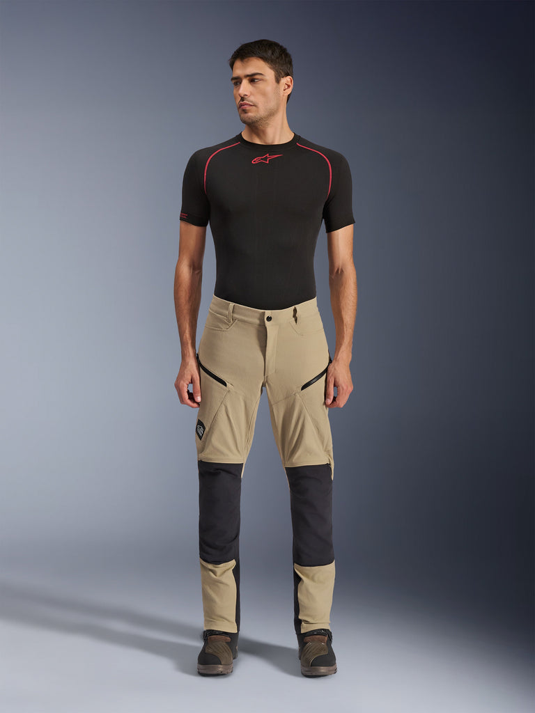 Alpinestars Flex-AST Explorer Pants, adventure motorbroek, beige en zwart, met versterkte kniepanelen, cargozakken met ritssluiting en ripstop-constructie, gedragen door een model in een studio-opname van voren.