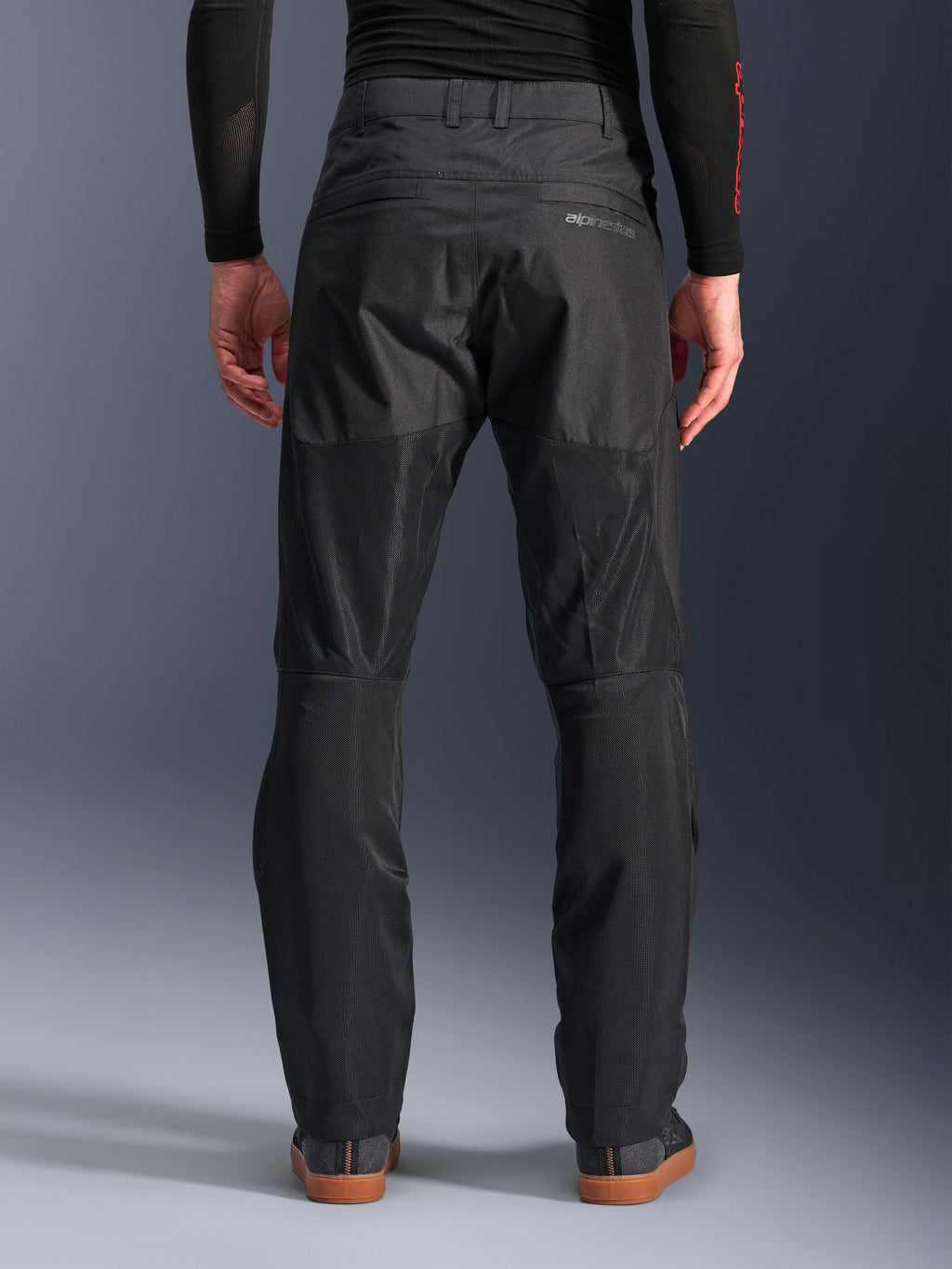 Alpinestars C-1 Air Pants, achteraanzicht, zwart, urban textiele motorbroek met grote tech mesh panelen aan de achterzijde van de benen voor ventilatie, strak ontwerp met subtiele branding, gedragen met een zwarte basislaag en casual motorschoenen.