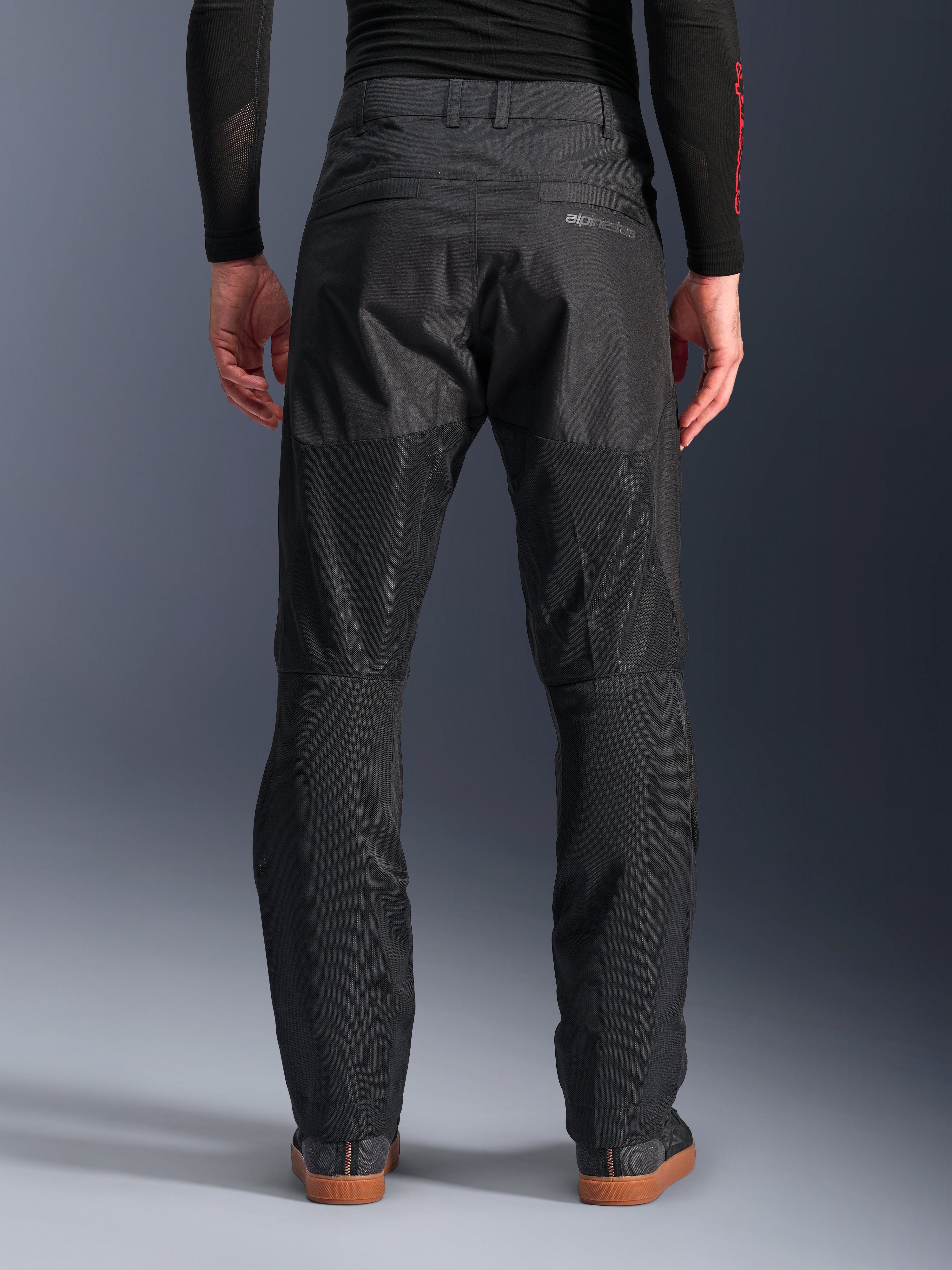 Alpinestars C-1 Air Pants, achteraanzicht, zwart, urban textiele motorbroek met grote tech mesh panelen aan de achterzijde van de benen voor ventilatie, strak ontwerp met subtiele branding, gedragen met een zwarte basislaag en casual motorschoenen.