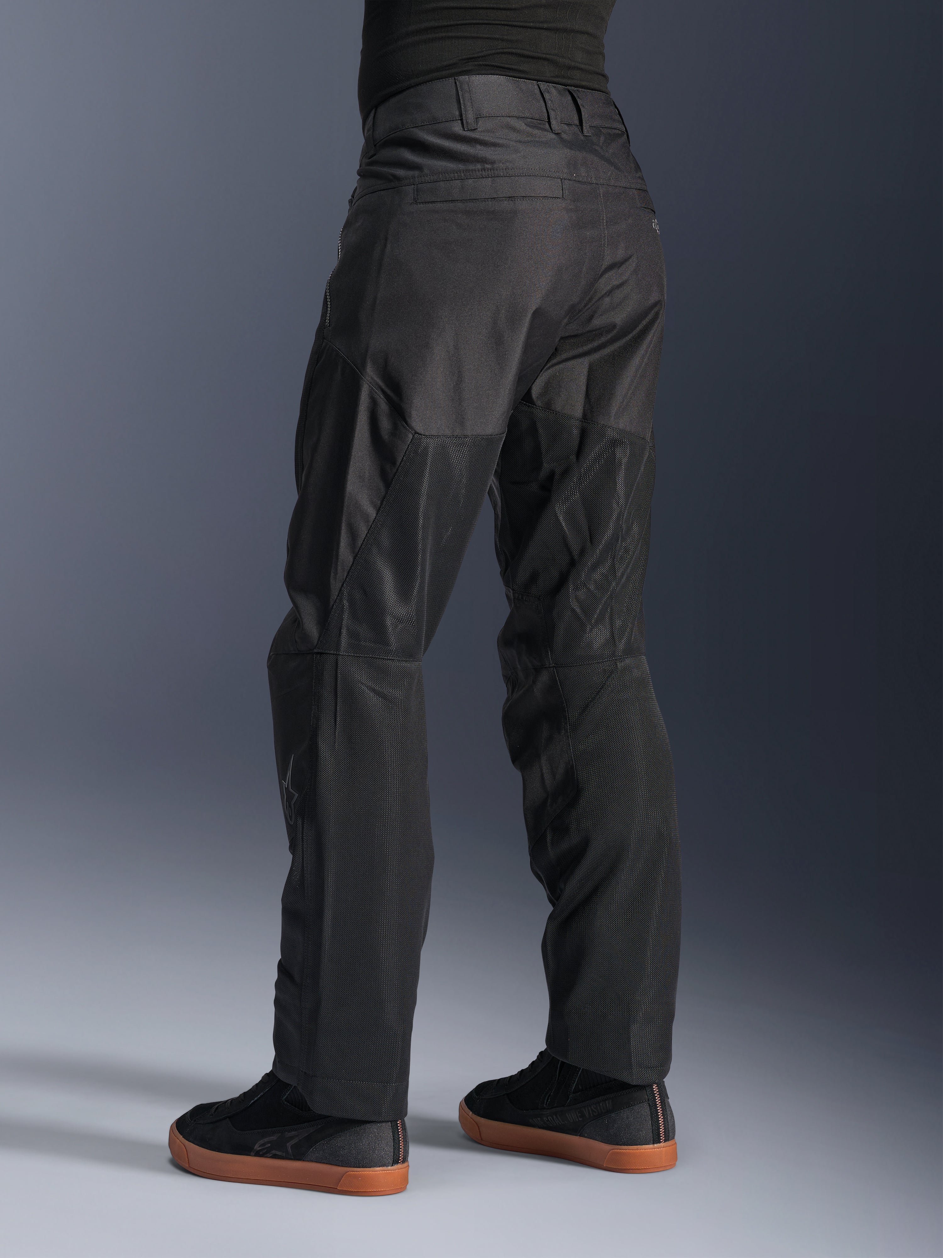 Alpinestars C-1 Air broek, stedelijke motorbroek, zwart, achteraanzicht met grote tech mesh-panelen aan de achterkant van de benen voor ventilatie, strakke styling voor stadsritten, gedragen met casual zwarte sneakers