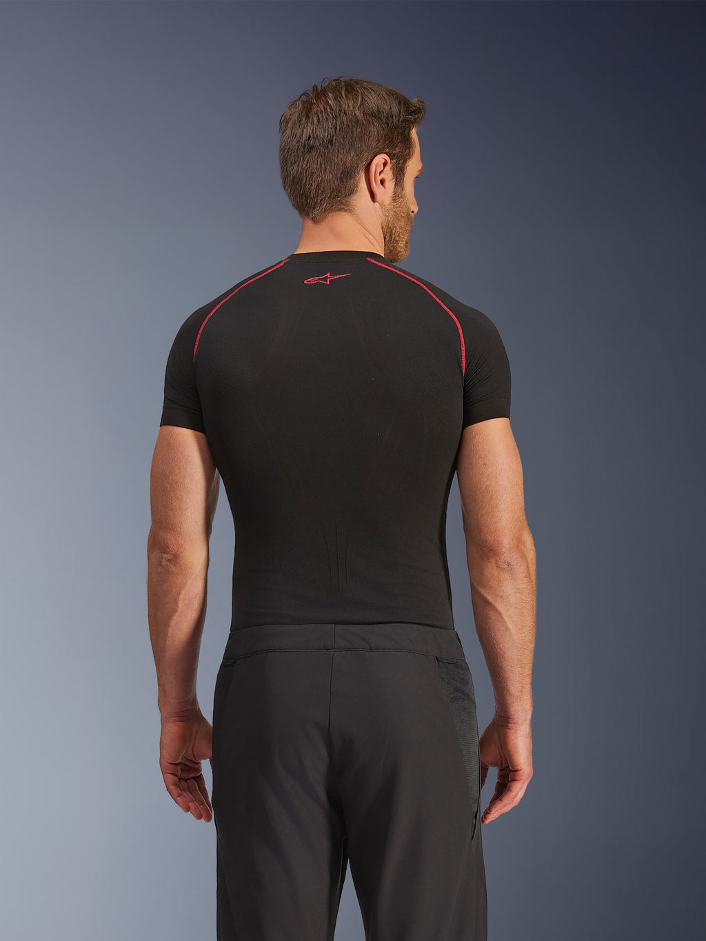 Achteraanzicht van een model in Alpinestars Aeroshell Airflow broek, zwart, lichtgewicht softshell constructie met geïntegreerde mesh zijpanelen, gecombineerd met een zwarte basislaag met rood contraststiksel, sportieve motorkleding