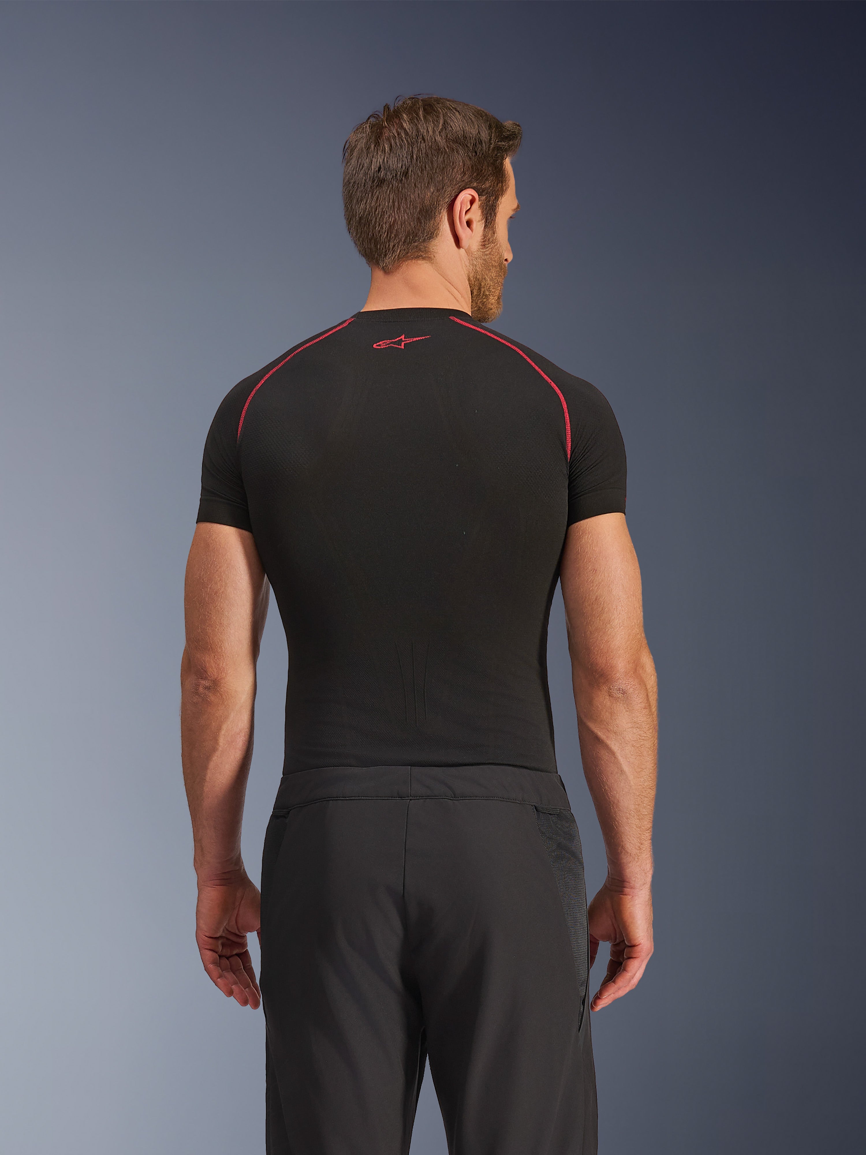 Achteraanzicht van een model in Alpinestars Aeroshell Airflow broek, zwart, lichtgewicht softshell constructie met geïntegreerde mesh zijpanelen, gecombineerd met een zwarte basislaag met rood contraststiksel, sportieve motorkleding