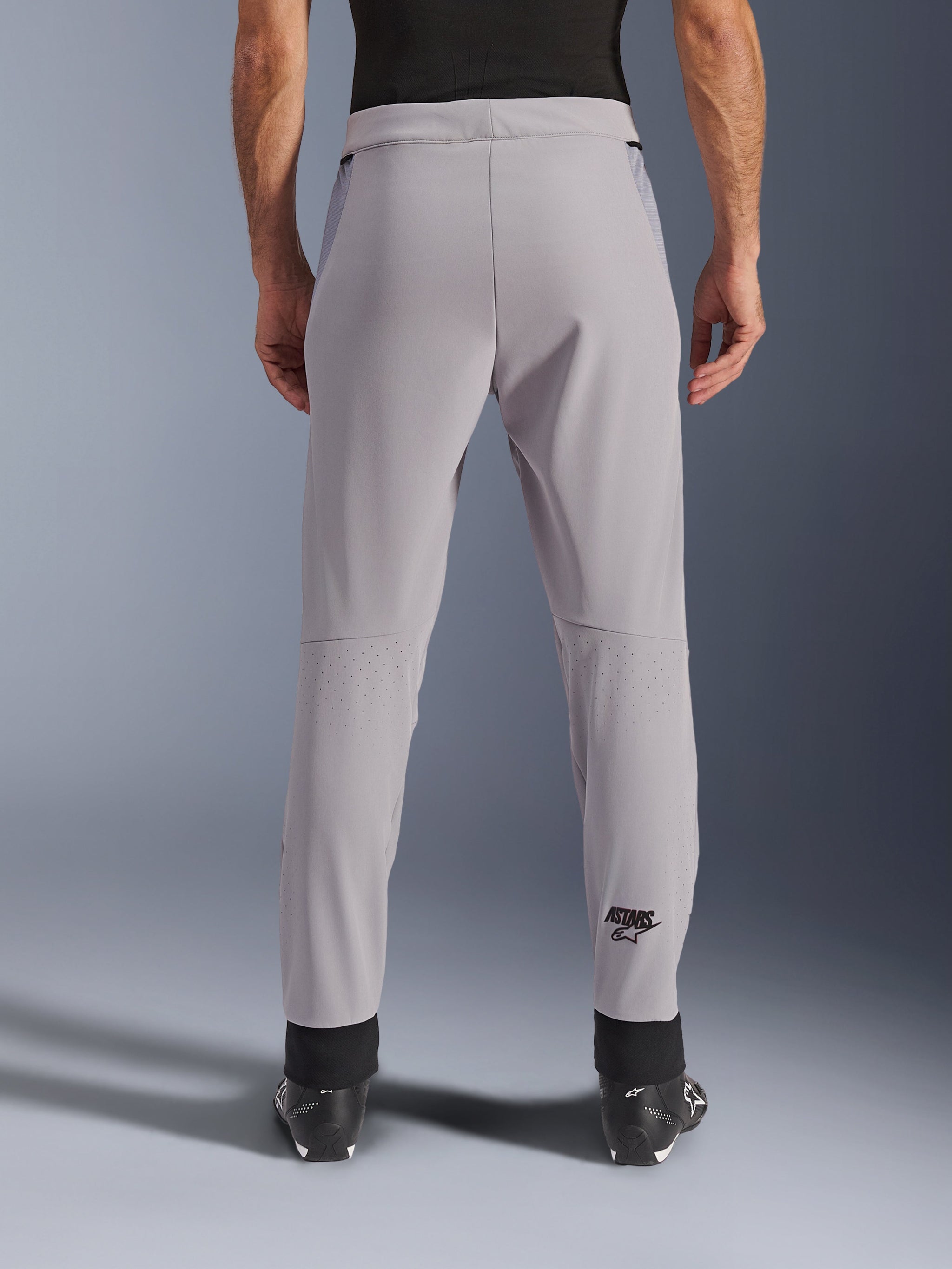Alpinestars Aeroshell Airflow Pants, motorbroek, Mid Gray, achteraanzicht met laser-geperforeerde zones op de kuiten en zwart Astars-logo, textiele softshell-constructie met zwarte enkelmanchetten en mesh heuppanelen