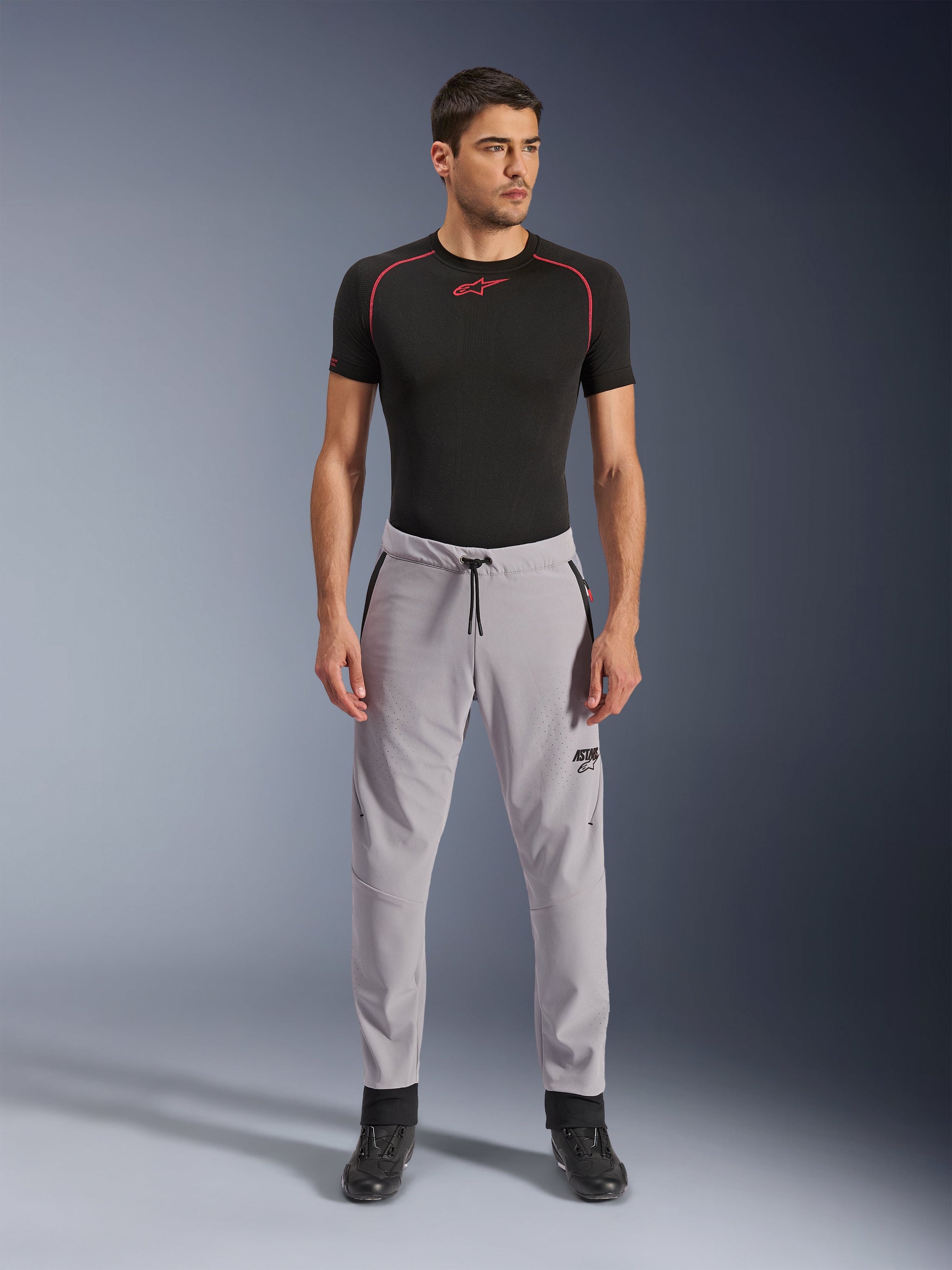 Alpinestars Aeroshell Airflow broek, Mid Gray, lichtgewicht textiele broek met laser-geperforeerde ventilatiezones en een tailleband met trekkoord, gedragen door een model met een zwart compressieshirt en zwarte motorlaarzen, strak en modern sportief design