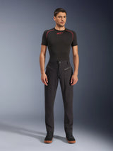 Alpinestars Flex-AST Canvas Pants, urban motorbroek, zwart, gedragen door een model met een zwarte basislaag met korte mouwen en rode stiksels en zwarte casual sneakers, waarbij de voorzakken met ritssluiting en het ergonomische canvas ontwerp worden geaccentueerd.