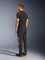 Alpinestars Flex-AST Canvas broek, Black Aluminum, stedelijke motorbroek, met tan zijpanelen met Alpinestars-branding, gedragen met een zwarte basislaag en sneakers, achteraanzicht met op werkkleding geïnspireerde styling en ergonomische motorpasvorm.