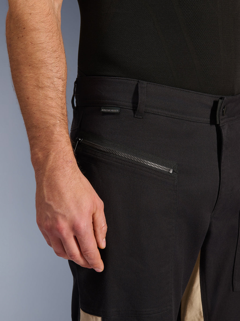 Alpinestars Flex-AST Canvas broek in Black Aluminum, close-up van de heupzone met een horizontale rijzak met ritssluiting, riemlussen en een klein merklabel, duurzame stretch polykatoen constructie voor urban motorrijden.