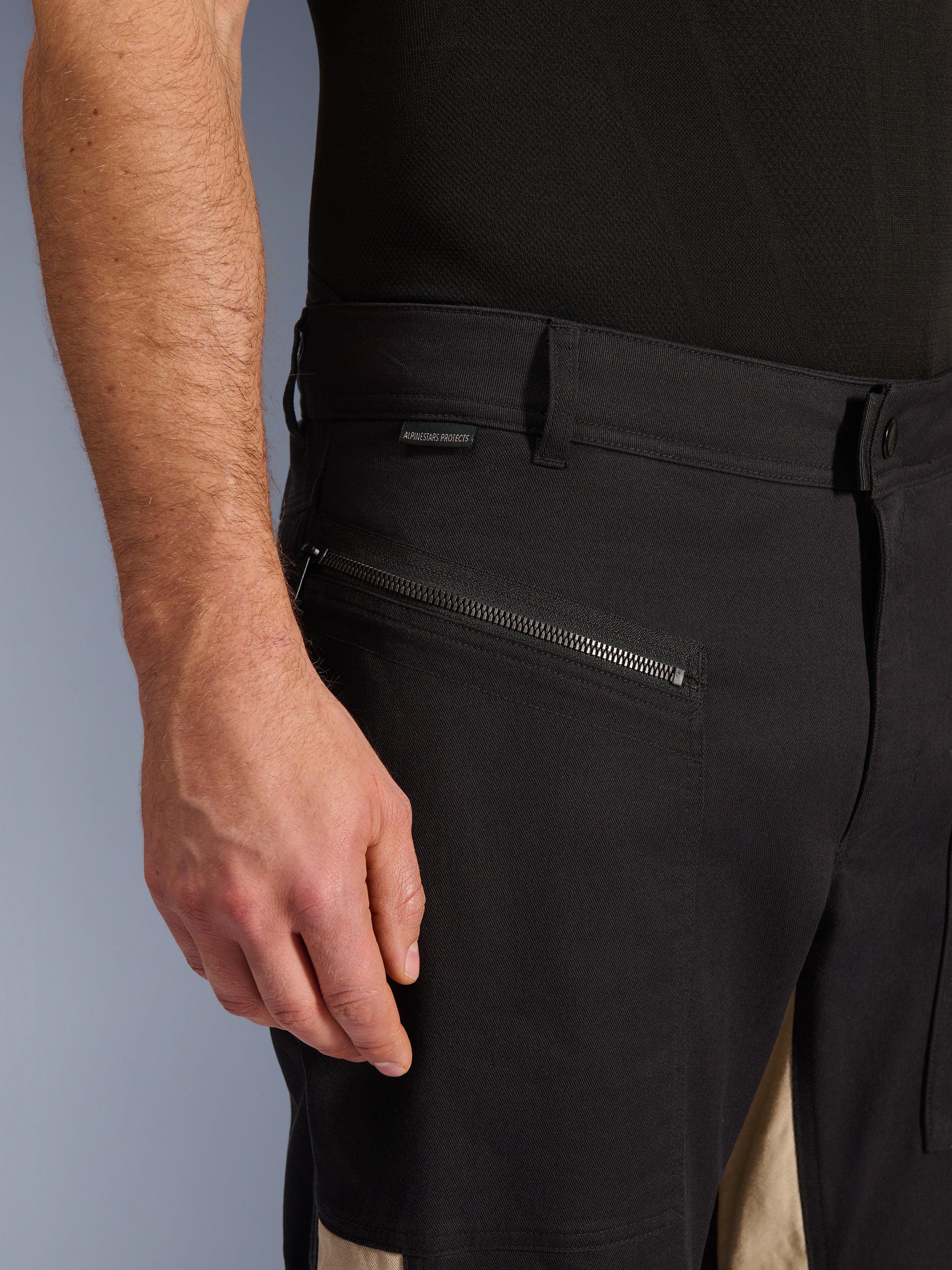 Alpinestars Flex-AST Canvas broek in Black Aluminum, close-up van de heupzone met een horizontale rijzak met ritssluiting, riemlussen en een klein merklabel, duurzame stretch polykatoen constructie voor urban motorrijden.