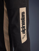 Alpinestars Flex-AST Canvas Pants, close-up detail of the side leg, Black with Aluminum tan accent panel, featuring a vertical black Alpinestars logo and star icon, durable polycotton twill for urban motorcycle riding