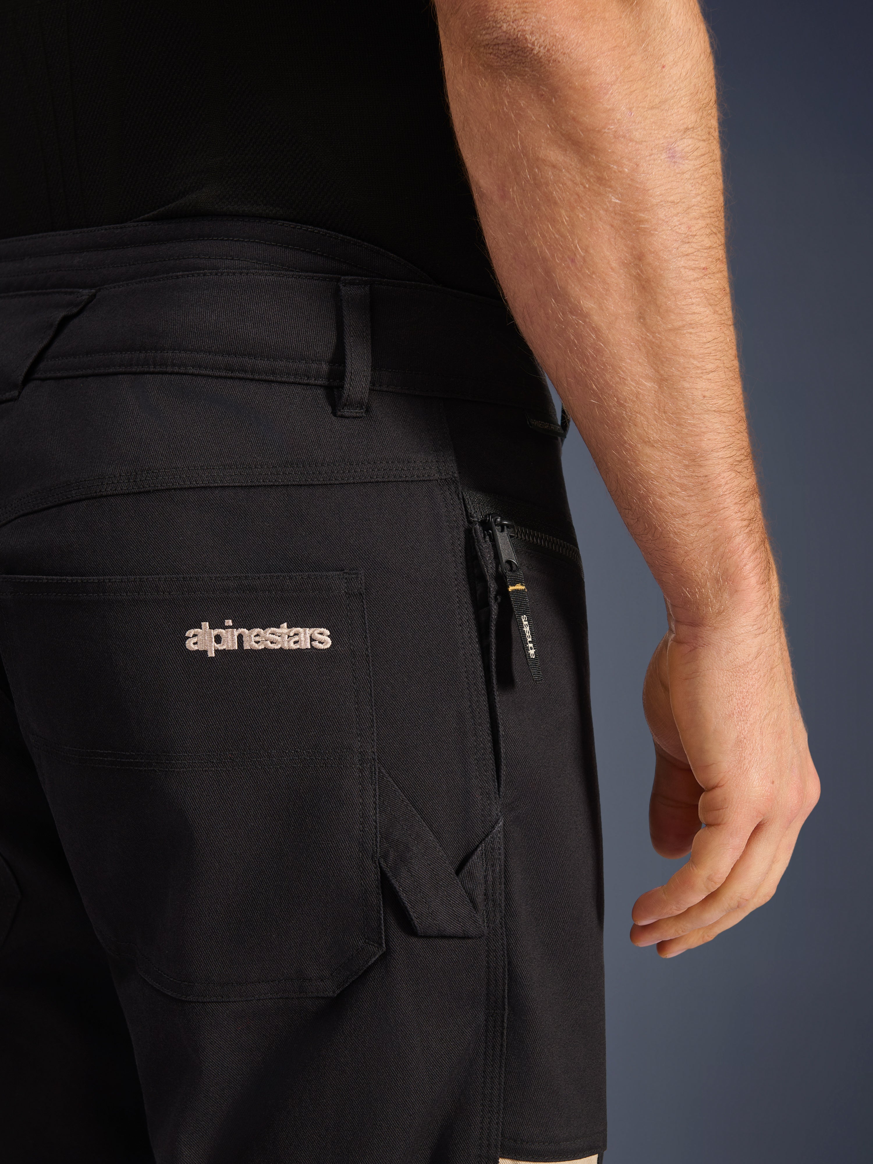 Alpinestars Flex-AST Canvas Broek, urban motorbroek, Black Aluminum, close-up van de achter- en zijzakken met geborduurd Alpinestars-logo, ritszak met merk-puller, duurzame stretch canvas twill constructie.