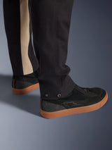 Alpinestars Flex-AST Canvas Pants in Black Aluminum, close-up of lower leg showing snap adjusters at the opening and a vertical aluminum-colored stripe, paired with black riding sneakers with gum soles, urban motorcycle apparel.