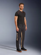 Alpinestars Flex-AST Canvas broek, urban motorbroek, Black Aluminum, gedragen met een zwarte technische basislaag en zwarte sneakers, voorzien van beige zijpanelen met verticale Alpinestars-branding, utilitair op werkkleding geïnspireerd ontwerp met voorgevormde knieën en metalen ritsen