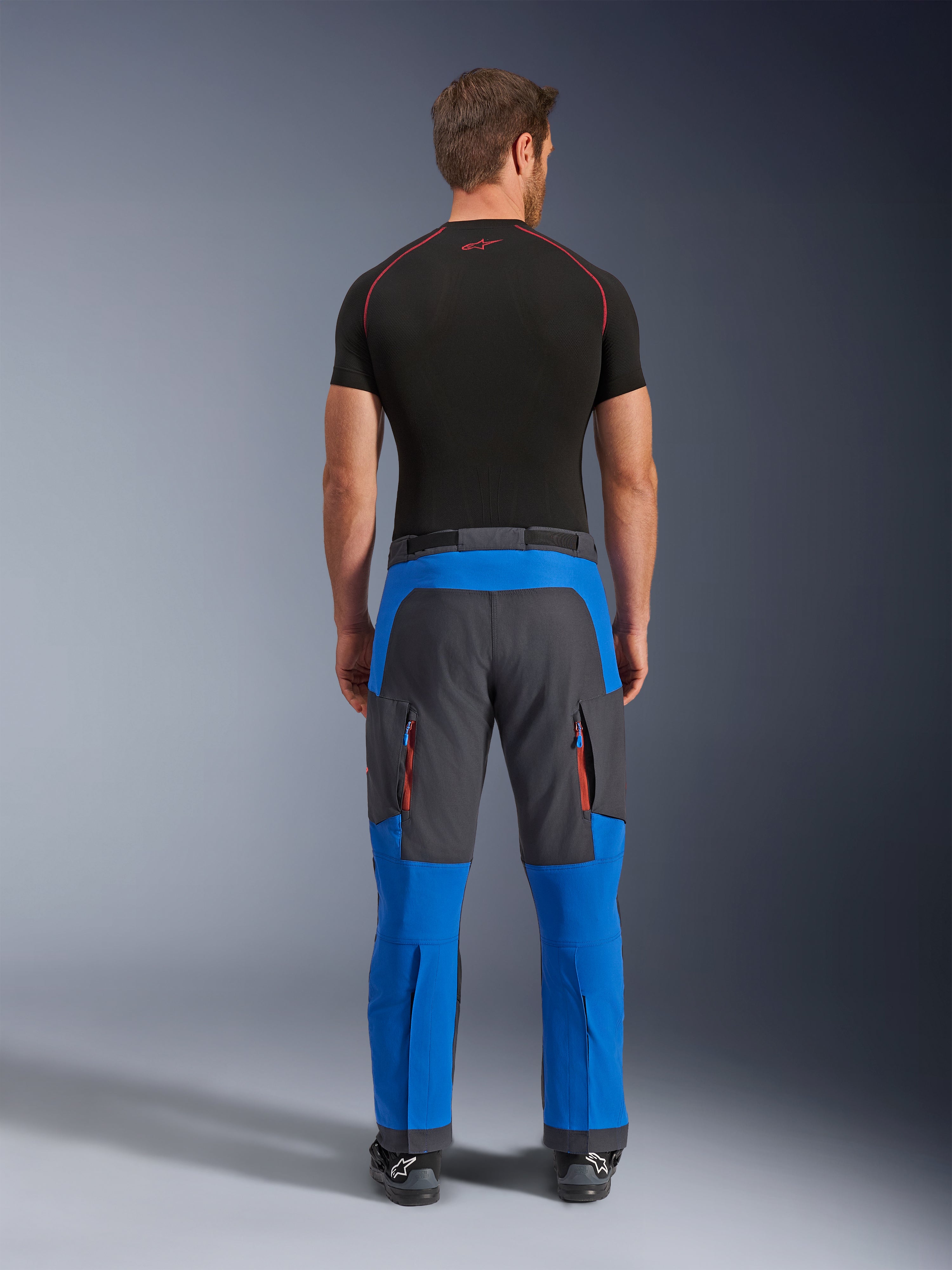 Alpinestars Maxdura Dual broek in Royal Blue en Deep Gray, adventure motorbroek, achteraanzicht, voorzien van cargozakken met rits en oranje accenten en een over-de-laars ontwerp, gedragen met een zwarte basislaag met korte mouwen