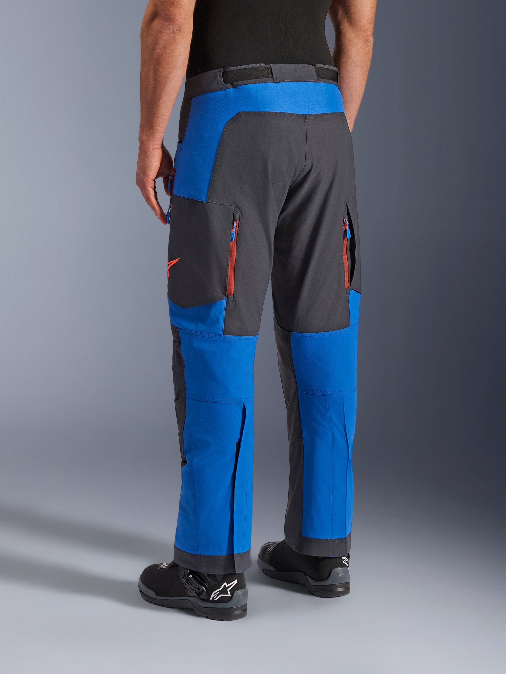 Alpinestars Maxdura Dual broek, Royal Blue en Deep Gray, achteraanzicht met ritszakken en ventilatiezones, over-de-laars ontwerp gedragen met zwarte Alpinestars laarzen, duurzame adventure en dual-sport motorkleding
