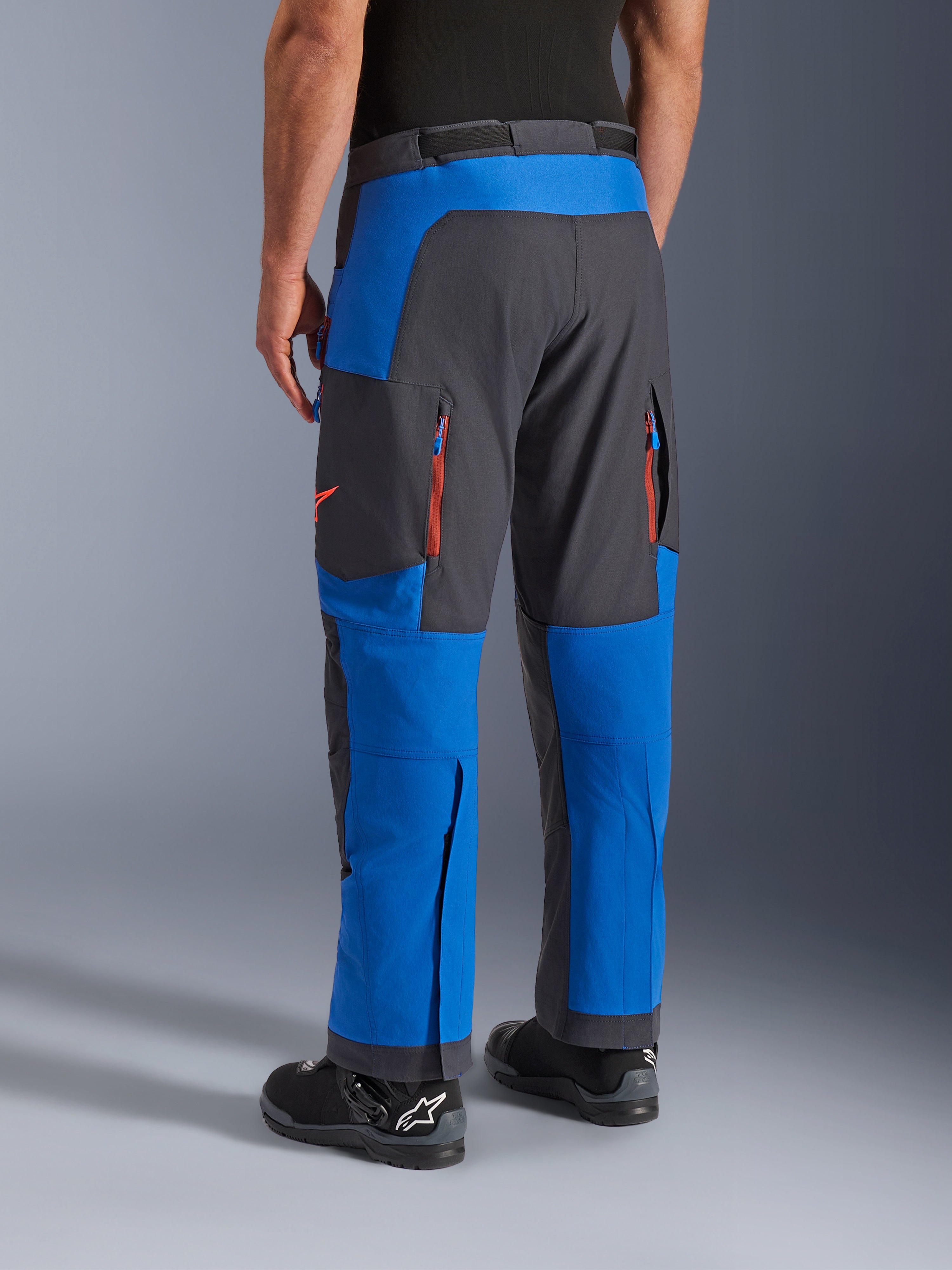 Alpinestars Maxdura Dual broek, Royal Blue en Deep Gray, achteraanzicht met ritszakken en ventilatiezones, over-de-laars ontwerp gedragen met zwarte Alpinestars laarzen, duurzame adventure en dual-sport motorkleding