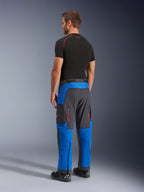 Alpinestars Maxdura Dual broek, adventure motorbroek, koningsblauw en diepgrijs, achter- en zijaanzicht gedragen door een model, met oranje ventilatieopeningen met rits, over-de-laars adventure pasvorm en duurzaam stretchmateriaal.