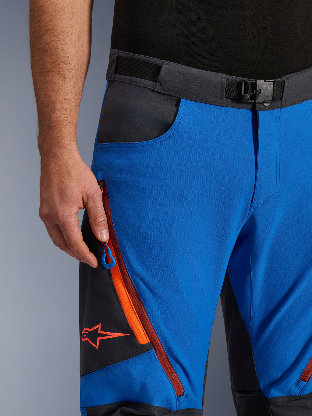 Alpinestars Maxdura Dual broek in Royal Blue en Deep Gray, close-up van de tailleband met magnetische gesp, cargozak met ritssluiting met oranje details en rood Alpinestars-logo, technische adventure motorkleding