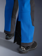 Alpinestars Maxdura Dual broek, Royal Blue en Deep Gray, close-up van verstelbare onderpijp met drukknoopsluitingen en inzetstuk, over-de-laars adventure pasvorm, gedragen met zwarte Alpinestars motorlaarzen