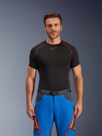 Alpinestars Maxdura Dual Pants, koningsblauw en diepgrijs, adventure motorbroek met oranje accenten, gedragen door model met een zwart compressieshirt, voorzien van een riem met magnetische gesp en dijbeenventilatie met rits, professionele motorsportkleding