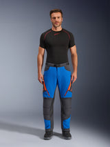 Alpinestars Maxdura Dual Pants, adventure motorbroek, koningsblauw en donkergrijs met oranje ritsaccenten, gedragen met een zwarte Alpinestars basislaag en zwarte laarzen, voorzien van verstevigde kniepanelen en een technisch off-road ontwerp