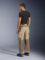 Alpinestars Maxdura Dual Pants, adventure- en dual-sport motorbroek, Walnut Aluminum, achteraanzicht gedragen door een model met een zwarte basislaag en motorlaarzen, voorzien van een multi-paneel constructie met ventilatieopeningen met rits aan de achterzijde en versterkte overlays.