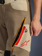 Alpinestars Maxdura Dual broek, Walnut en Aluminum, detailopname van de dij met een groot diagonaal ventilatiesysteem met ritssluiting, rode accenten en een rood Alpinestars-logo op een beige paneel, adventure motorkleding