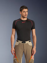 Alpinestars Maxdura Dual Pants in Walnut Aluminum, bruine en beige adventure motorbroek gedragen door een model met een zwart ondershirt, voorzien van oranje dijventilatie met rits, rode logo's en een magnetische gespsluiting, studioportret.