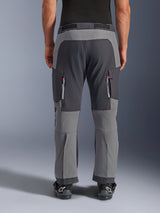 Alpinestars Maxdura Dual Pants, adventure motorbroek, donkergrijs en diepgrijs, achteraanzicht met de nadruk op de verstevigde zitvlak- en kniepanelen, ventilatieopeningen met rits op de bovenbenen, gedragen met zwarte Alpinestars laarzen, robuuste stretch polyamide constructie voor dual-sport rijden.