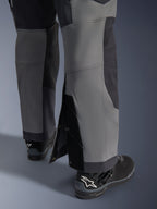 Alpinestars Maxdura Dual Pants, adventure motorbroek, donkergrijs en diepgrijs, close-up van de verstelbare over-de-laars broekzoom met drukknoopsluitingen en verstevigde panelen, gedragen met zwarte Alpinestars laarzen, robuust technisch ontwerp voor dual-sport ritten