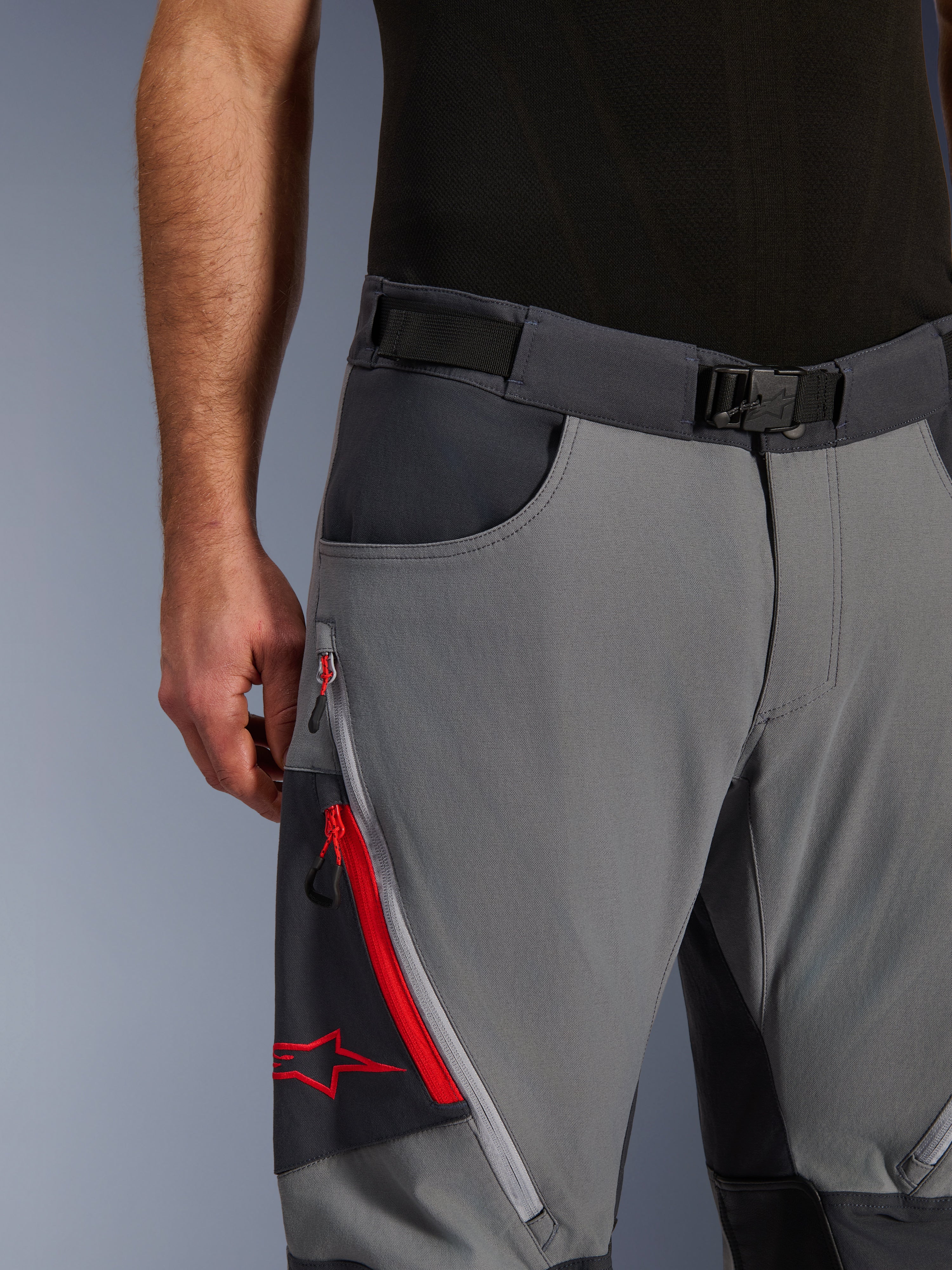 Alpinestars Maxdura Dual Pants, adventure motorbroek, donkergrijs en diepgrijs, close-up met verstelbare tailleband met magnetische gesp, cargozak met ritssluiting, rode details en Alpinestars-logo.