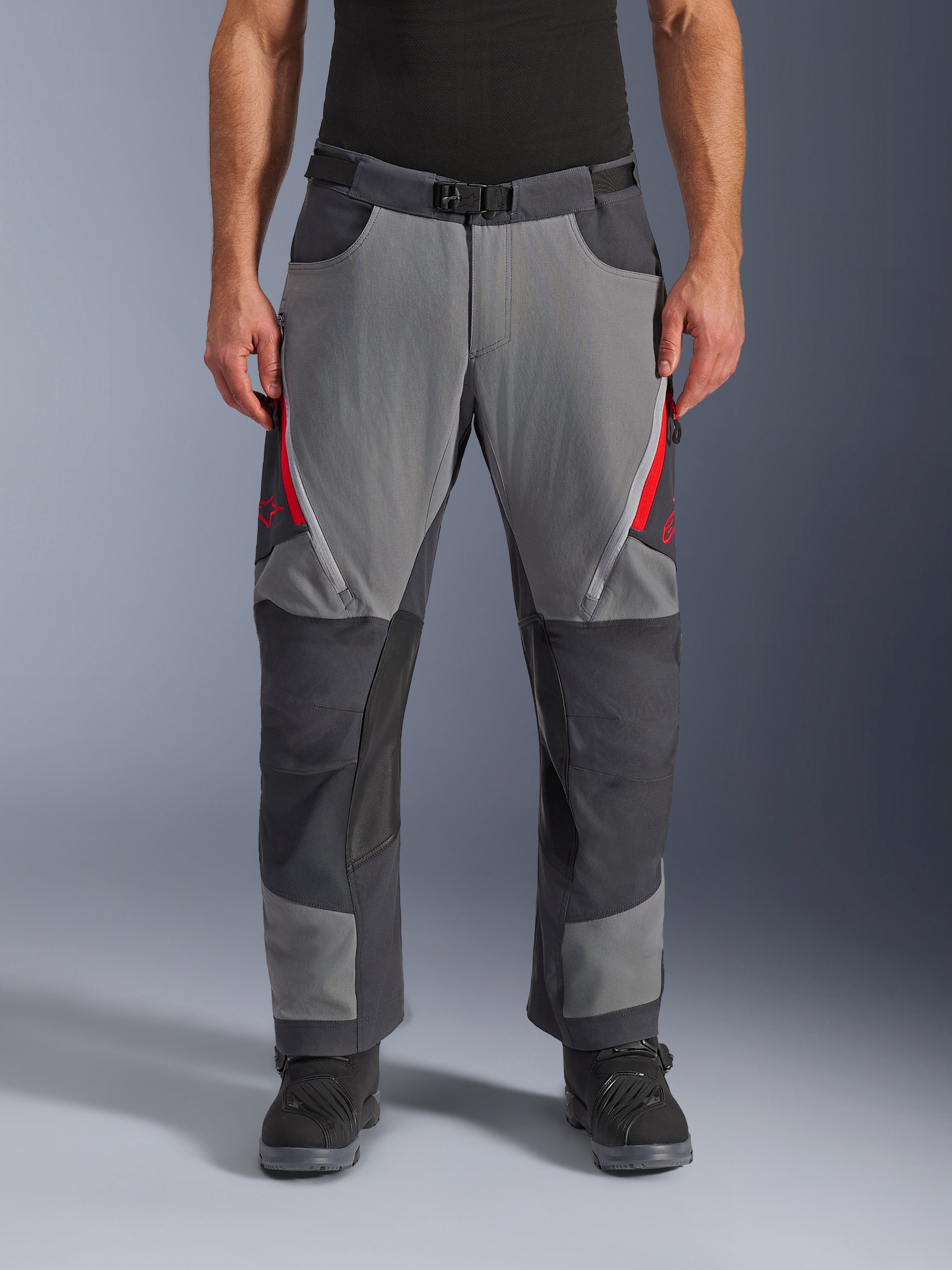 Alpinestars Maxdura Dual Pants, adventure motorbroek, donkergrijs en diepgrijs met rode accenten, vooraanzicht met dijventilatie met rits, magnetische gespsluiting en verstevigde kniepanelen, over-de-laars ontwerp voor dual-sport rijden.