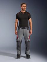 Alpinestars Maxdura Dual broek, motorbroek, donkergrijs en diepgrijs met rode accenten, vooraanzicht gedragen door een model met een zwarte Alpinestars base-layer en zwarte laarzen, voorzien van verstevigde panelen en ventilatieopeningen met rits op de bovenbenen, adventure-stijl motoruitrusting
