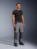 Alpinestars Maxdura Dual Pants, adventure motorbroek, donkergrijs en diepgrijs, gedragen met een zwarte basislaag en laarzen, voorzien van rode ventilatieopeningen met rits, versterkte panelen op de knieën en het zitvlak en een tailleband met riem, sportieve pasvorm voor dual-sport ritten