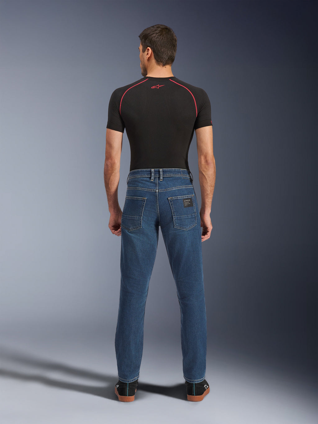 Alpinestars Flex-AST 5 Denim Broek, Indigo Washed blauw, achteraanzicht met taps toelopende urban pasvorm, gedragen door model met zwart performance t-shirt en sneakers, casual beschermende motorkleding