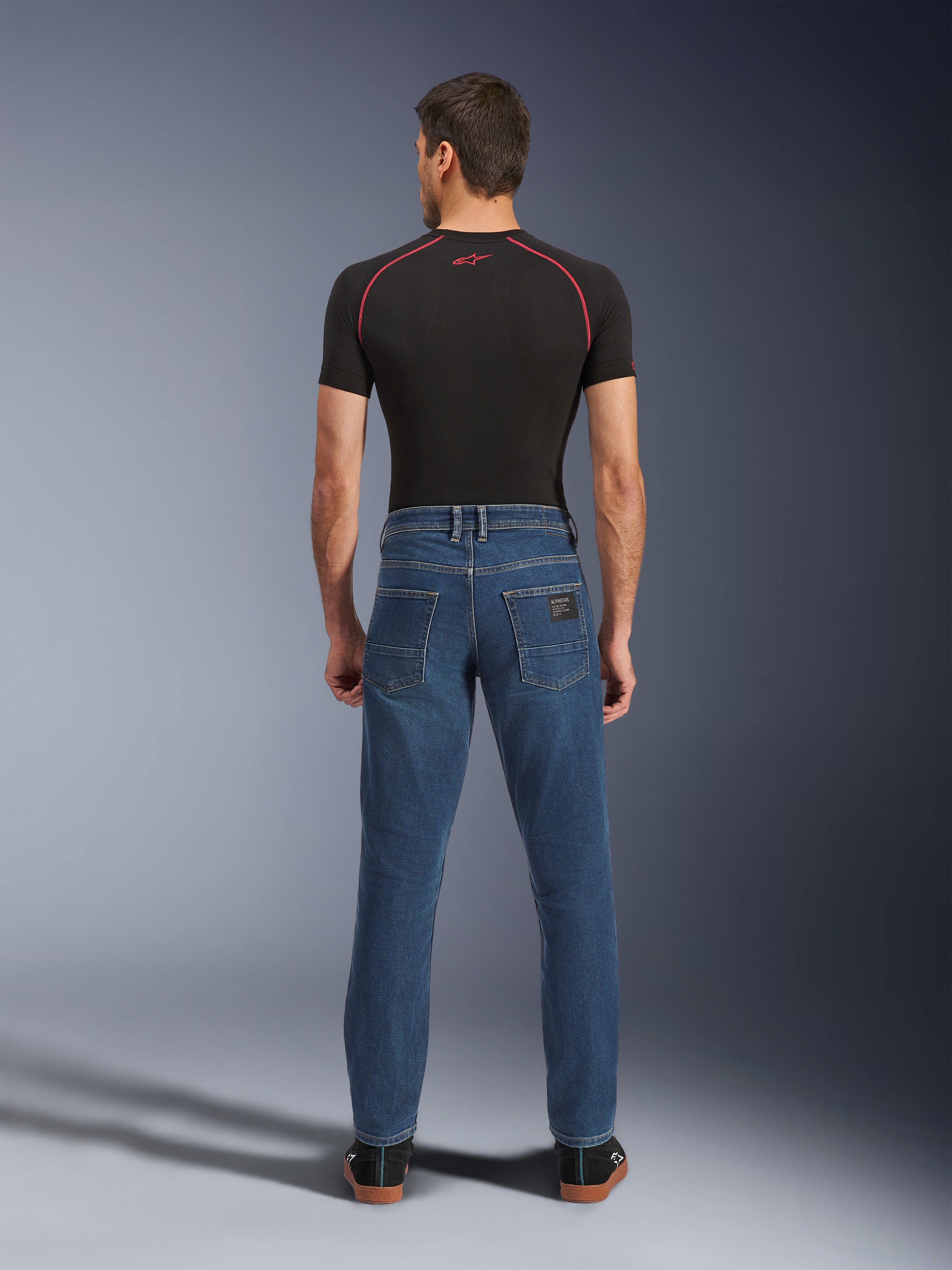 Alpinestars Flex-AST 5 Denim Broek, Indigo Washed blauw, achteraanzicht met taps toelopende urban pasvorm, gedragen door model met zwart performance t-shirt en sneakers, casual beschermende motorkleding