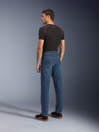 Alpinestars Flex-AST 5 Denim broek, Indigo Washed, stedelijke motorbroek met een toelopende pasvorm, van achteren getoond op een model met een zwart T-shirt en sneakers, voorzien van een strak vijfzakkenontwerp en monolaag stretchconstructie