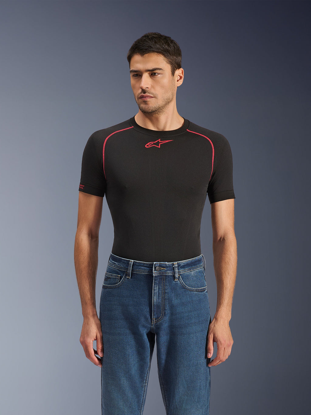 Alpinestars Flex-AST 5 Denim broek in Indigo Washed, stedelijke motorjeans met een toelopende pasvorm, gedragen door een mannelijk model met een zwarte basislaag met korte mouwen en rode accenten, casual road-to-street styling