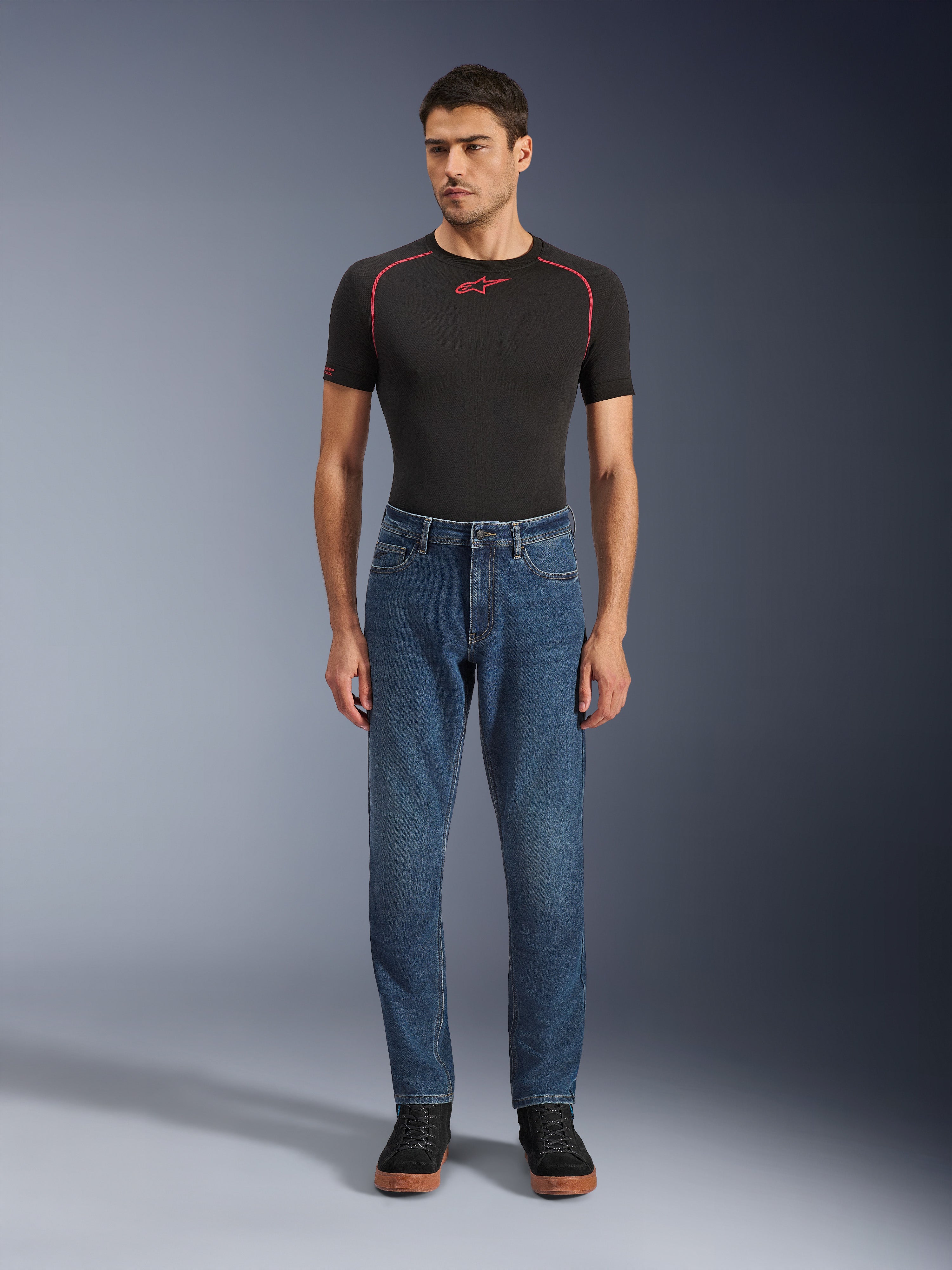 Alpinestars Flex-AST 5 Denim Pants, motorjeans, Indigo Washed, gedragen met een zwart performance t-shirt en zwarte sneakers, voorzien van een toelopende pasvorm en monolaag stretch-denim constructie voor stedelijk rijden