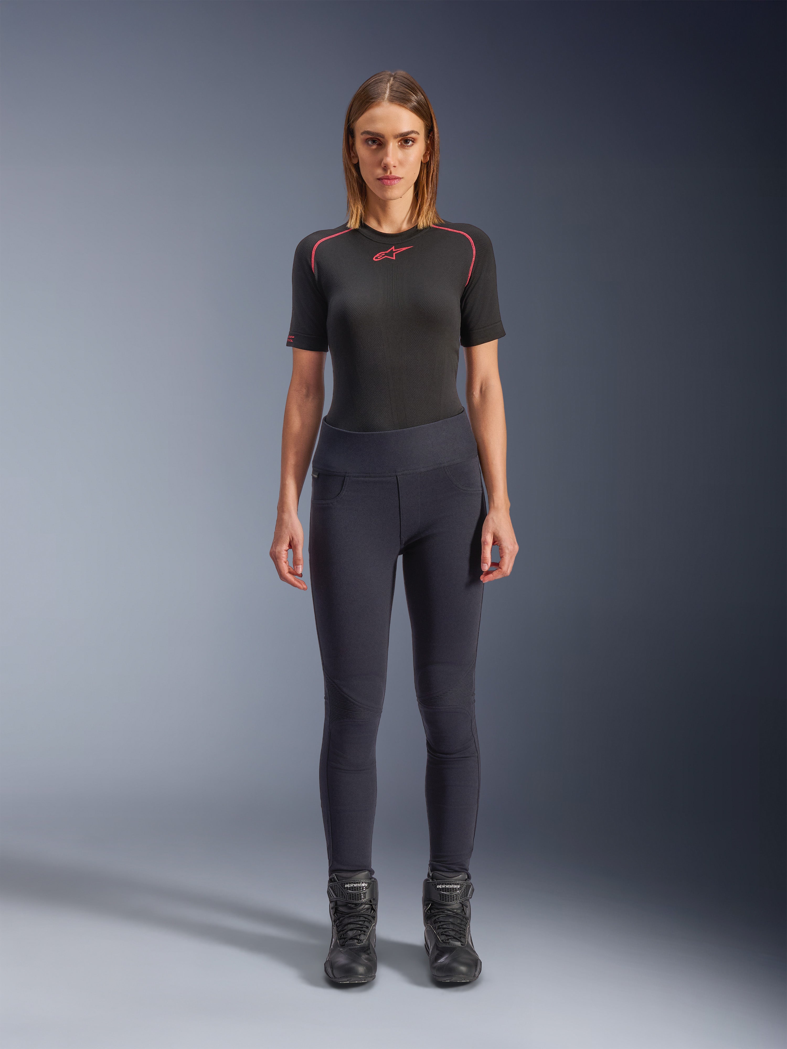 Alpinestars Stella Flex-AST Leggings, stedelijke motorleggings voor dames in het zwart, skinny model met hoge taille, gedragen met een zwart technisch shirt met korte mouwen en zwarte motorlaarzen, voorzien van harmonicavormige kniepanelen en een eigentijdse minimalistische look
