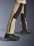 Alpinestars Stella Flex-AST Explorer dames motorbroek, adventure motorbroek, zandkleur en zwart, close-up van de onderbenen en enkels met een lange zijrits en zwarte verstevigingspanelen, gedragen met zwarte Alpinestars motorschoenen