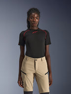 Alpinestars Stella Flex-AST Explorer Pants, dames motorbroek in zandkleur, gedragen met een zwarte technische top met korte mouwen en rode stiksels, adventure touring kleding voorzien van cargozakken met ritssluiting en duurzame ripstop stof