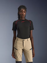 Alpinestars Stella Flex-AST Explorer Pants, dames motorbroek in zandkleur, gedragen met een zwarte technische top met korte mouwen en rode stiksels, adventure touring kleding voorzien van cargozakken met ritssluiting en duurzame ripstop stof