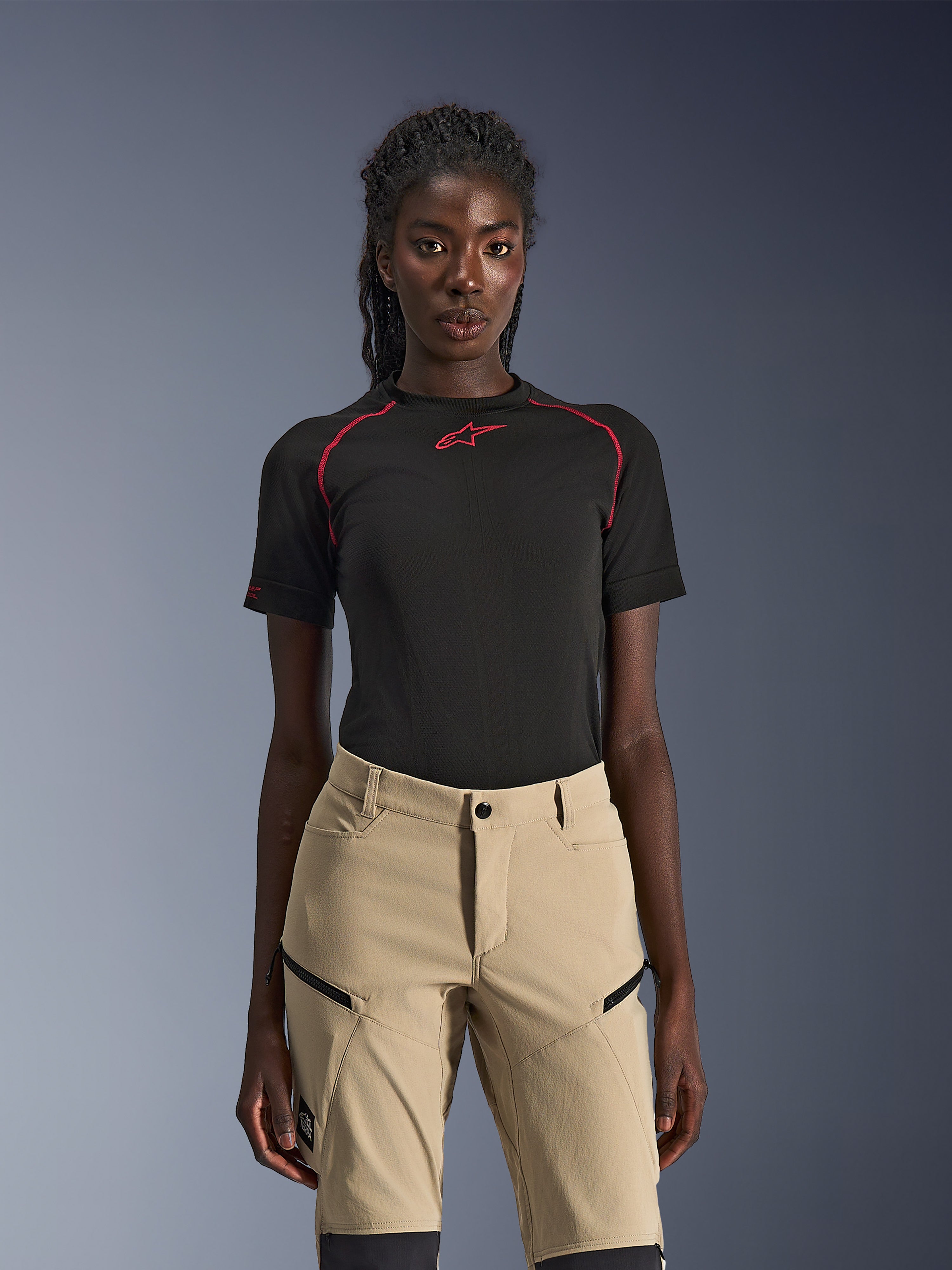 Alpinestars Stella Flex-AST Explorer Pants, dames motorbroek in zandkleur, gedragen met een zwarte technische top met korte mouwen en rode stiksels, adventure touring kleding voorzien van cargozakken met ritssluiting en duurzame ripstop stof